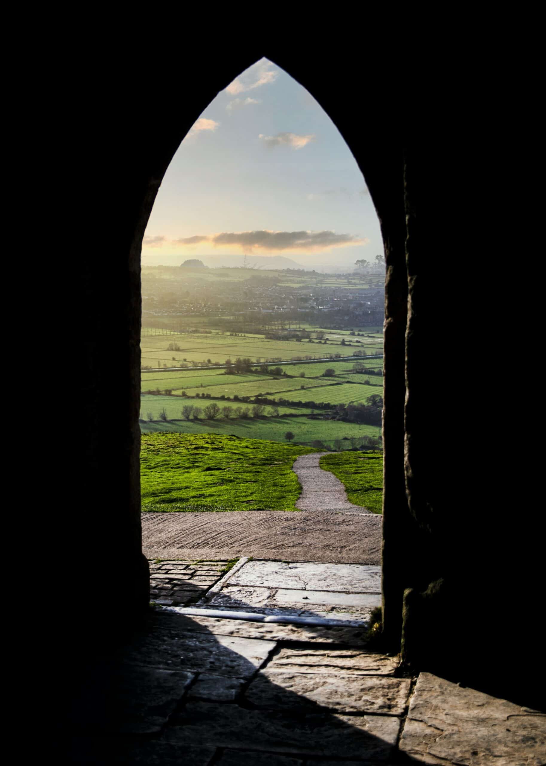 a doorway leading to a green field and far-off village